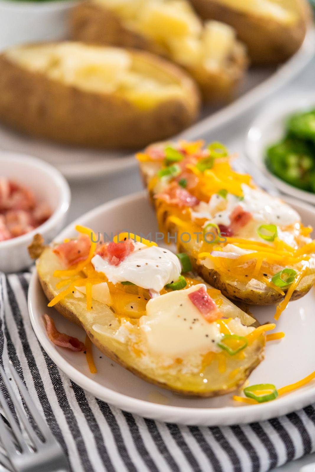 Pressure Cooker Baked Potatoes. Garnished large baked potatoes with butter, sour cream, cheese, and bacon bits on a white plate.