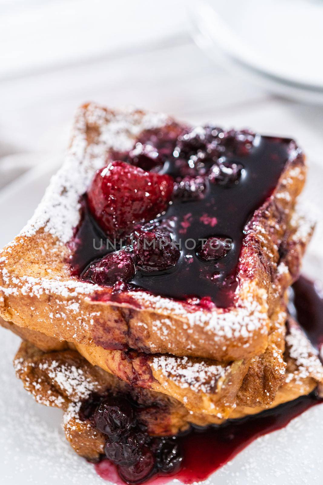 Stack of freshly made french toast garnished with mix berry compote and powder sugar.