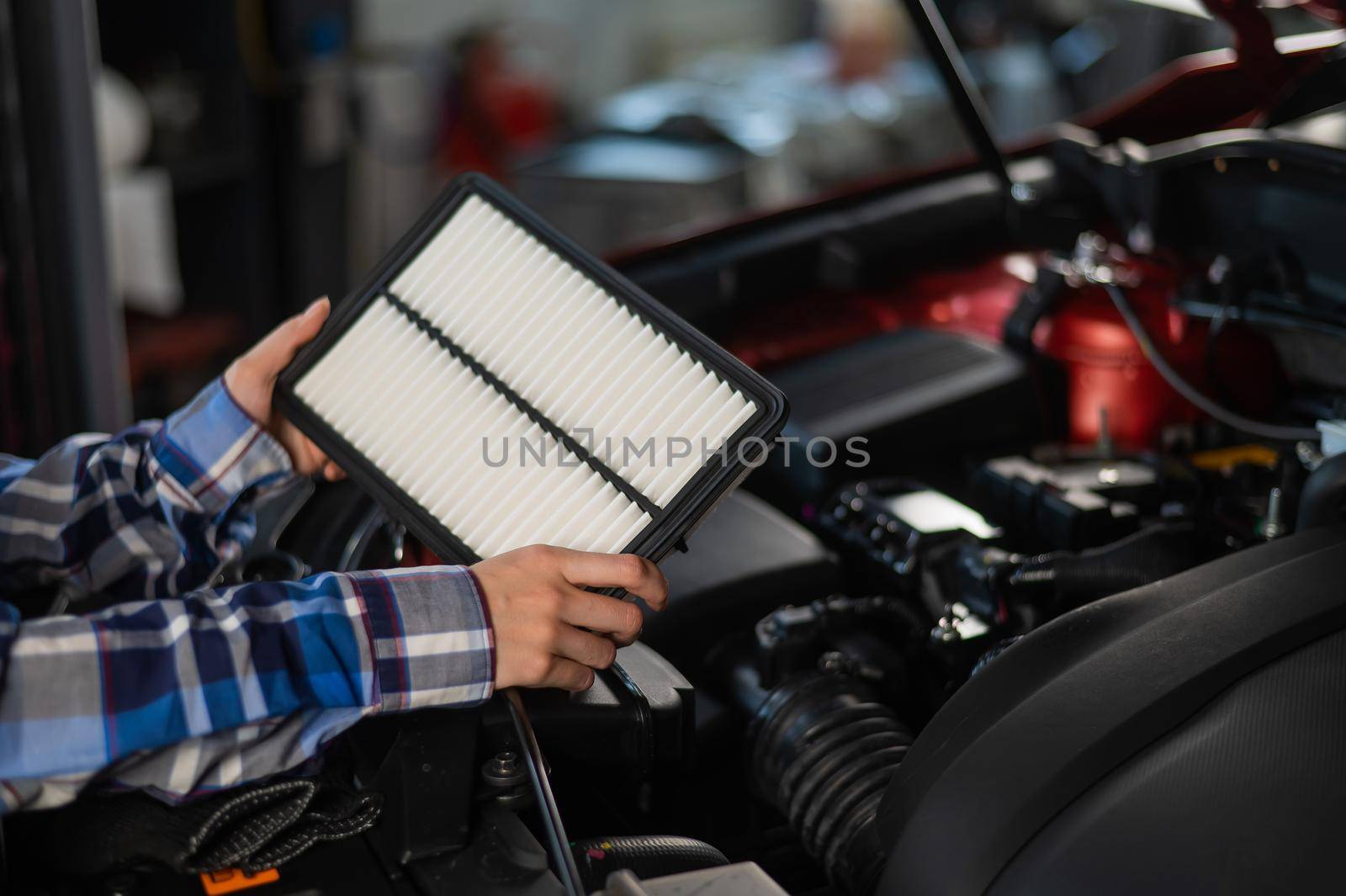 Caucasian female auto mechanic changes the engine air filter in the car