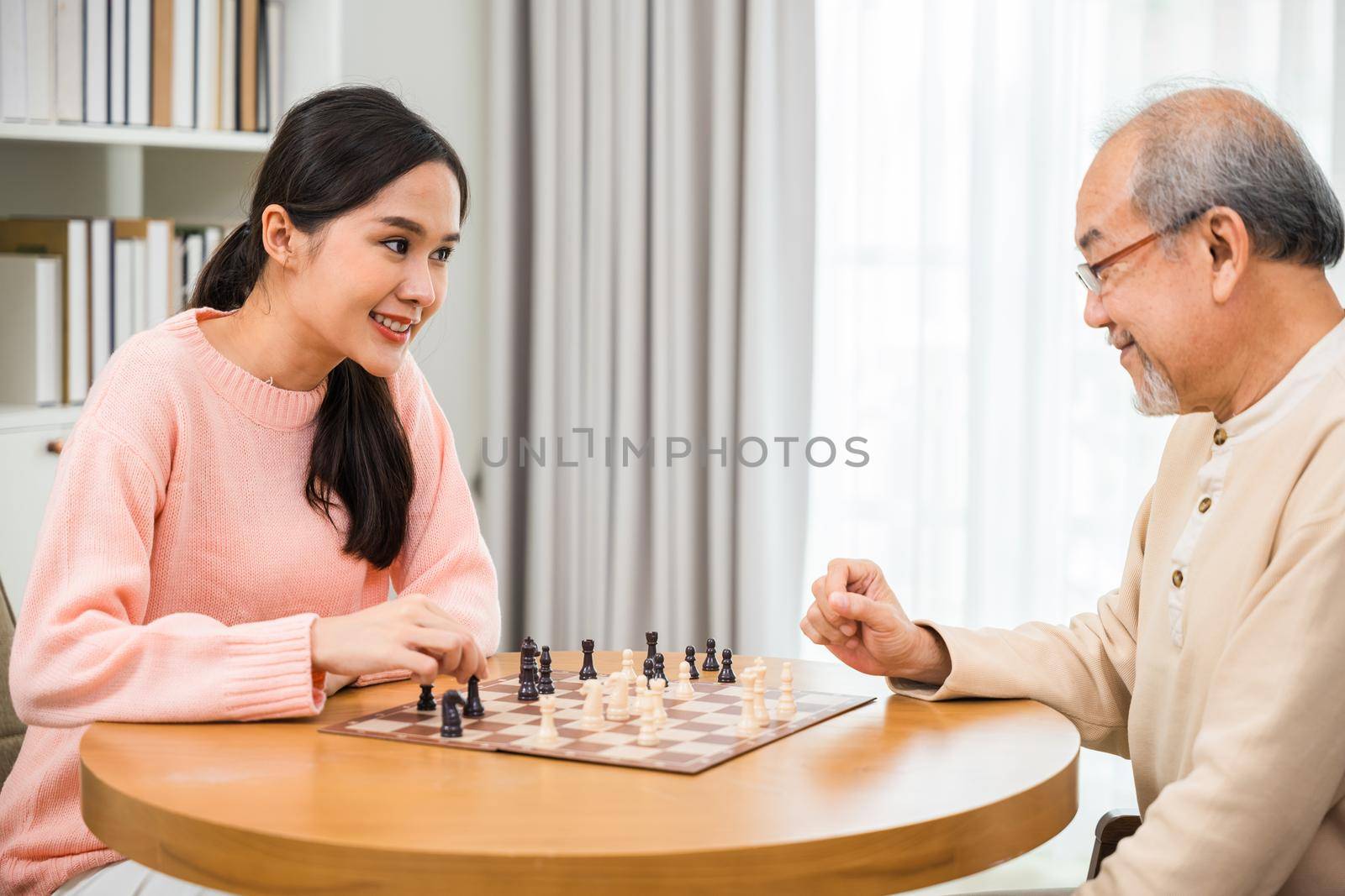 Beautiful young smile woman having fun sitting playing chess game with senior elderly at home, nurse caregiver in nursing home for leisure, Happy active retired people, Healthcare and medical concept