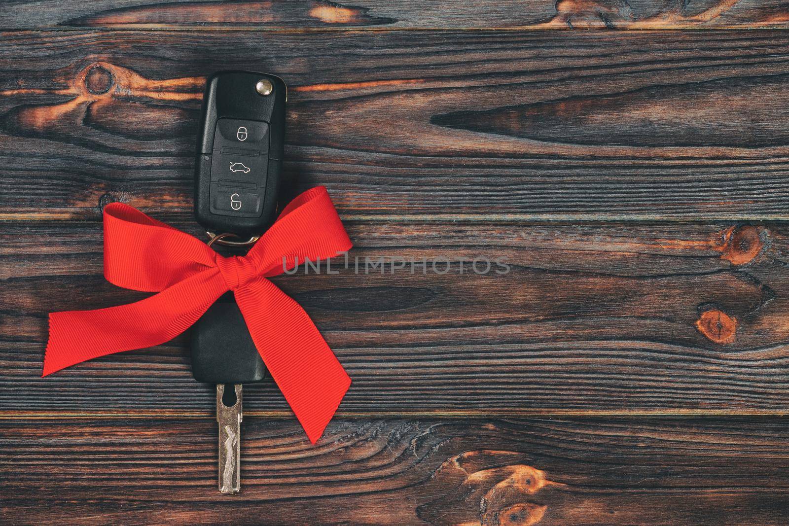 Close-up view of car keys with red bow as present on wooden vintage background.