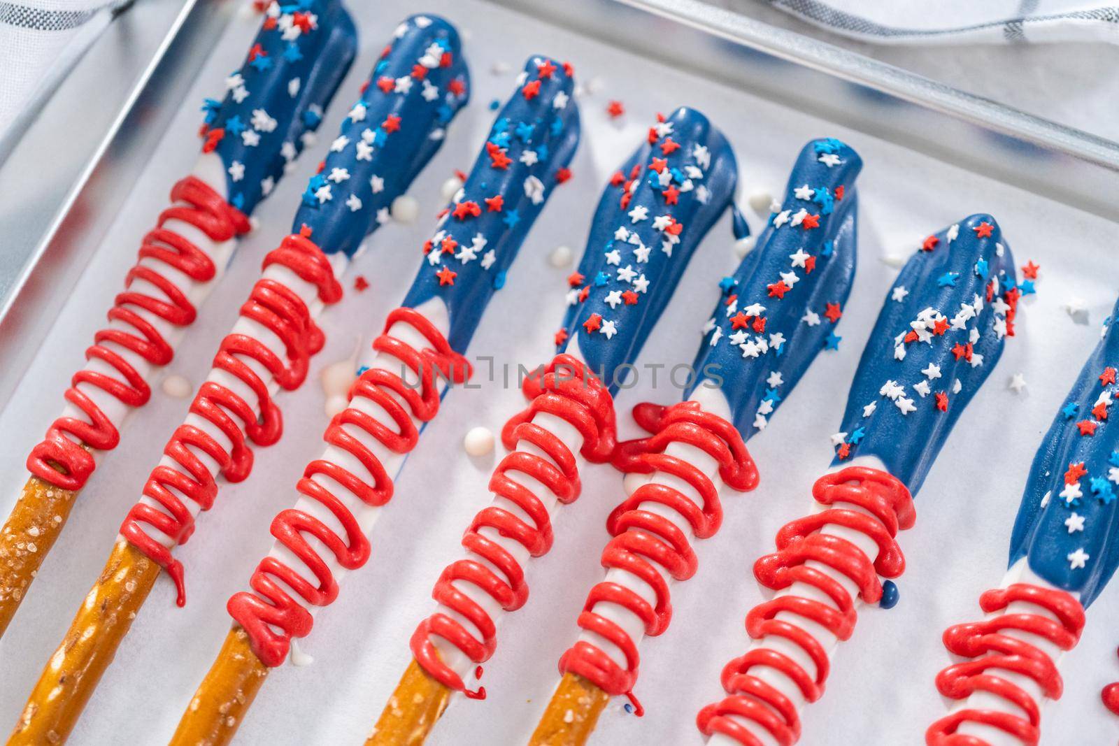 Homemade chocolate-covered pretzel rods decorated like the American flag drying on a baking sheet lined with parchment paper.