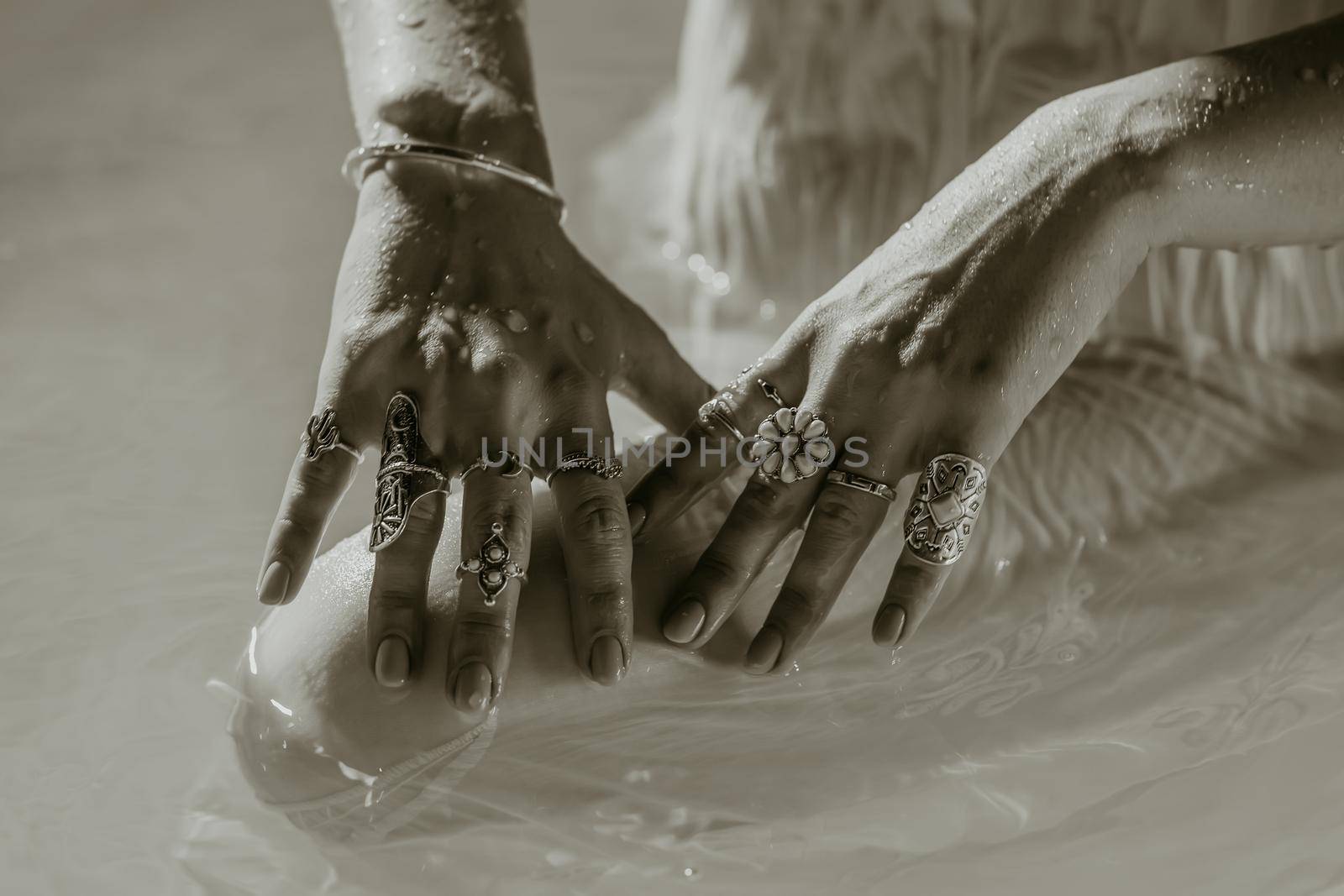 Beautiful gypsy woman demonstrates boho jewelry, rings with turquoise stones on hands. Black and white. Girl in white dress showing accessories in blue water. Femininity, trend, hippie style concept. by kristina_kokhanova