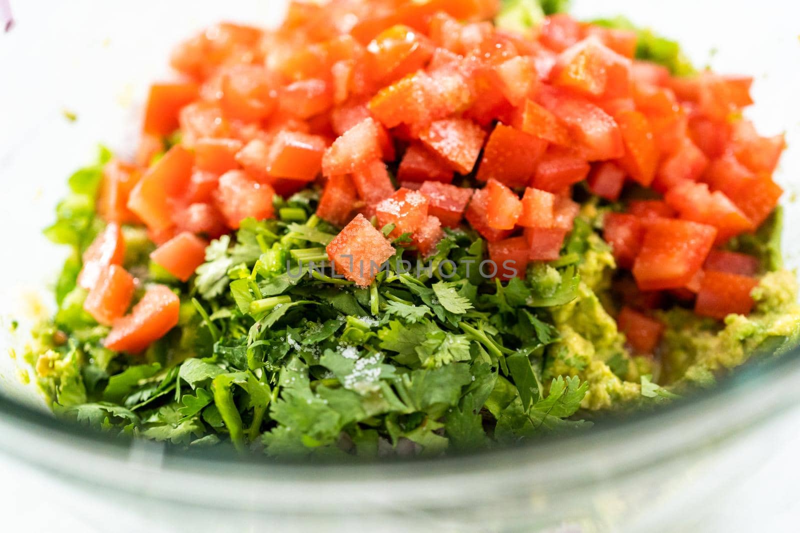 Mixing ingredients in a glass mixing bowl to prepare classic guacamole dip on the counter.