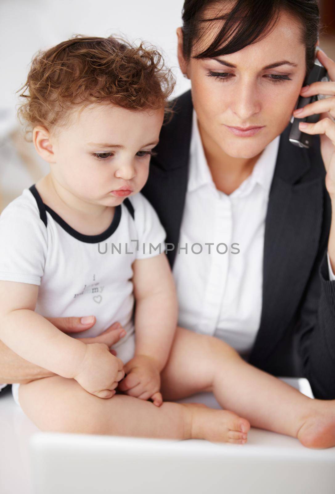 Being a working mom can be tricky...Young working mother talking on the phone while holding her baby