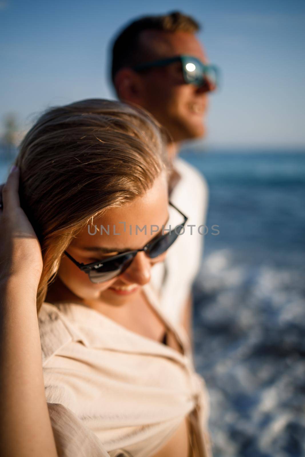 Young tanned woman in sunglasses walking along the sea coast with a man, selective focus