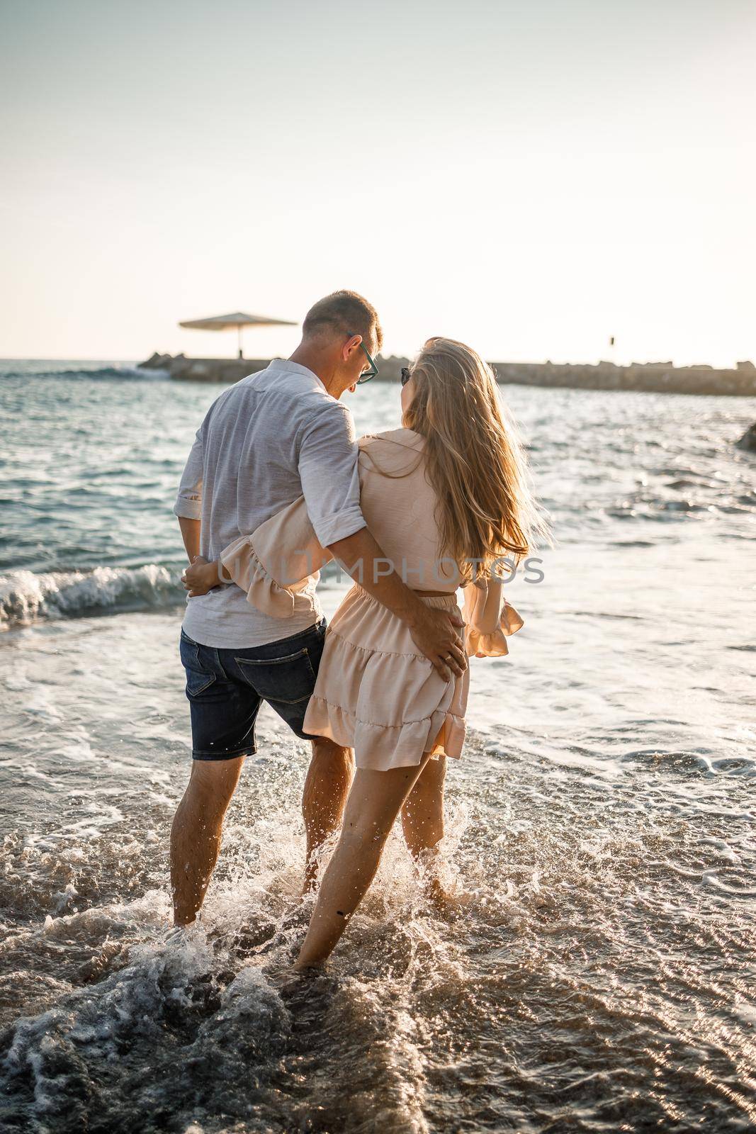 Summer holidays and travel. Sexy woman and man in sea water at sunset. Loving couple relax on the sunrise beach. Love relationship of a couple enjoying a summer day together by Dmitrytph