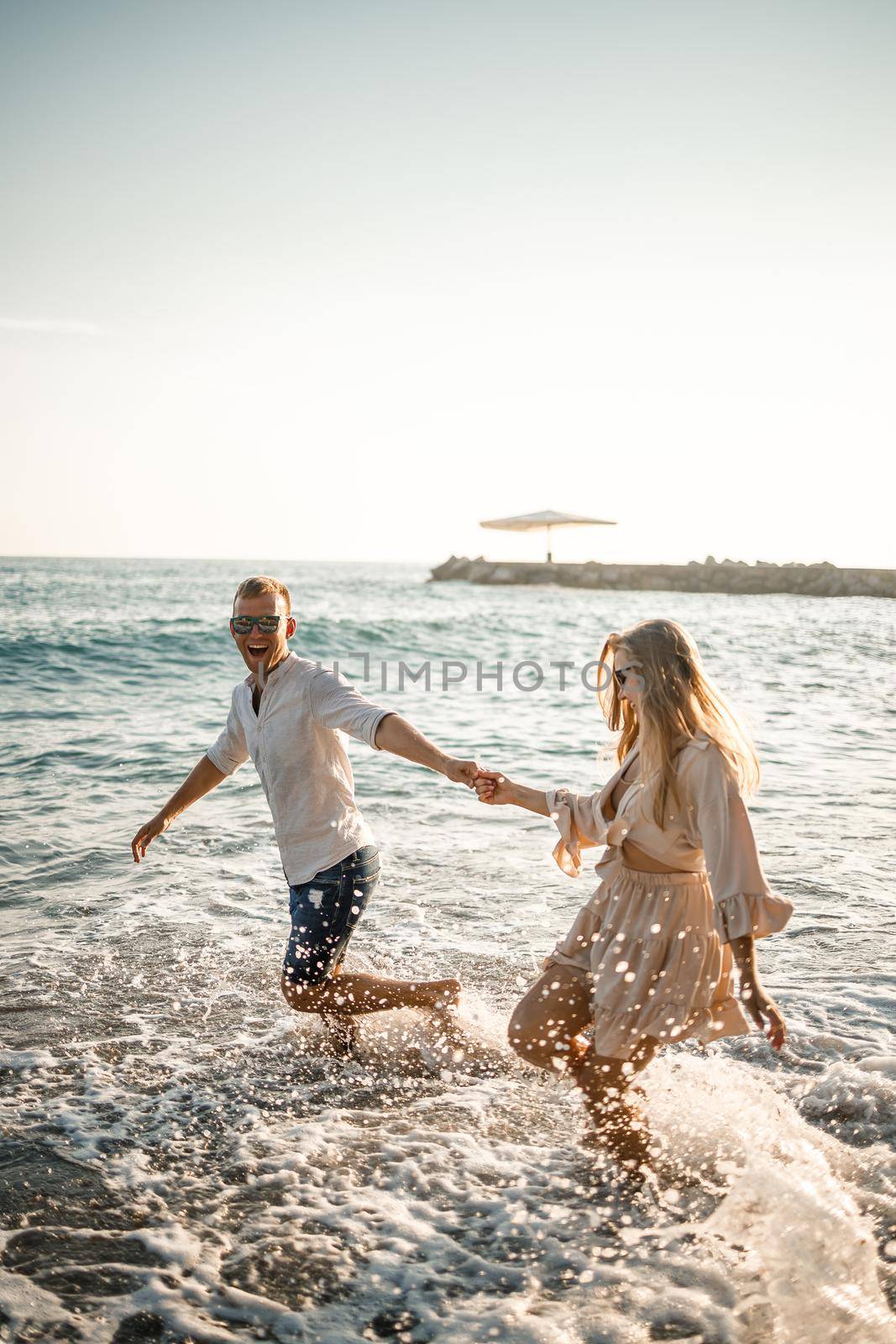 Summer holidays and travel. Sexy woman and man in sea water at sunset. Loving couple relax on the sunrise beach. Love relationship of a couple enjoying a summer day together by Dmitrytph