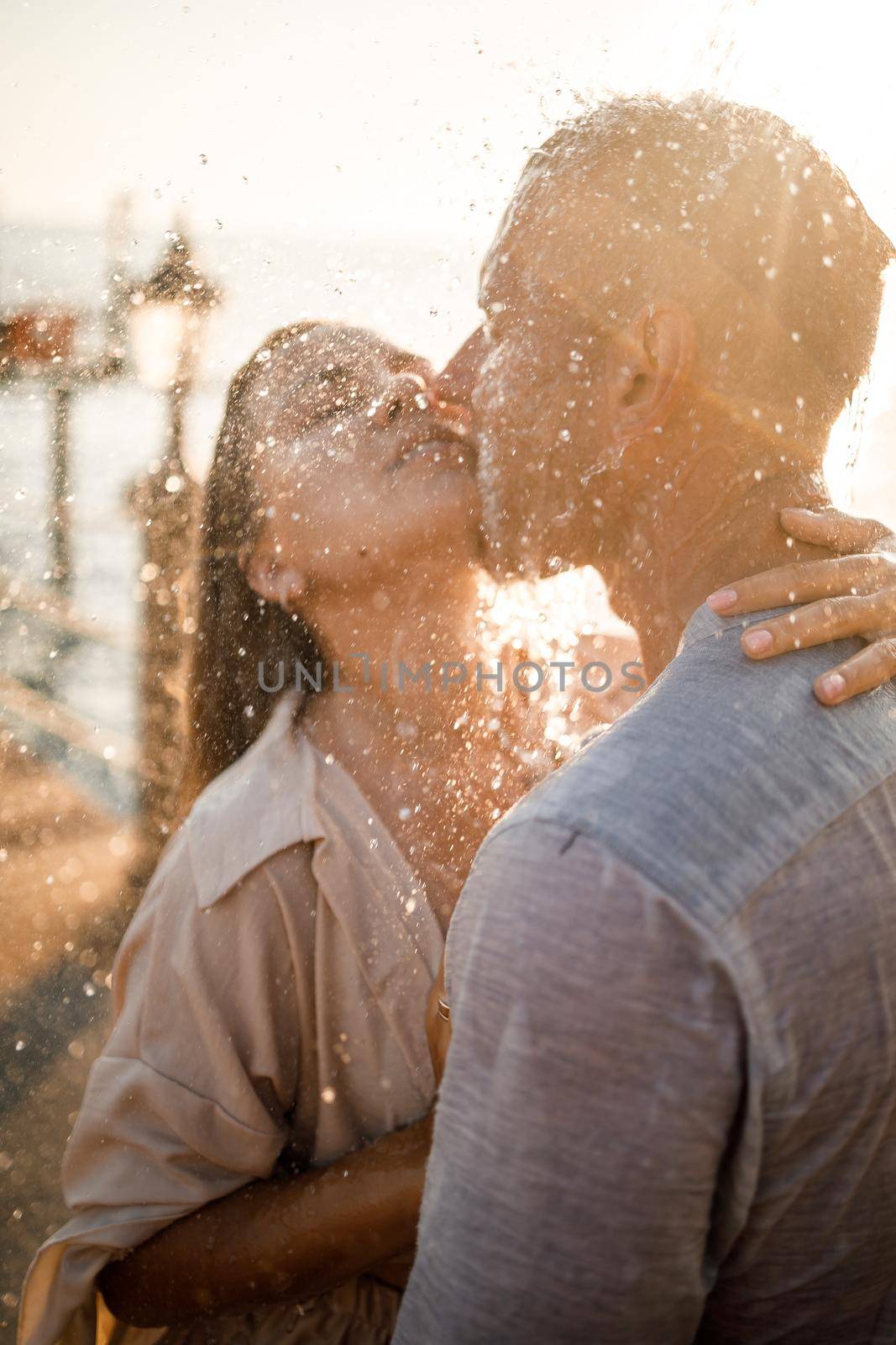 Beautiful couple in love hugs and kisses under the streams of water in a luxury spa hotel on their honeymoon, vacation in the tropics. Selective focus