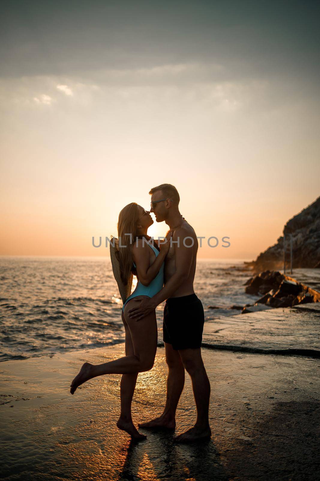 Beautiful couple in love on the background of the sunset by the sea. Young woman and man hugging by the sea at sunset