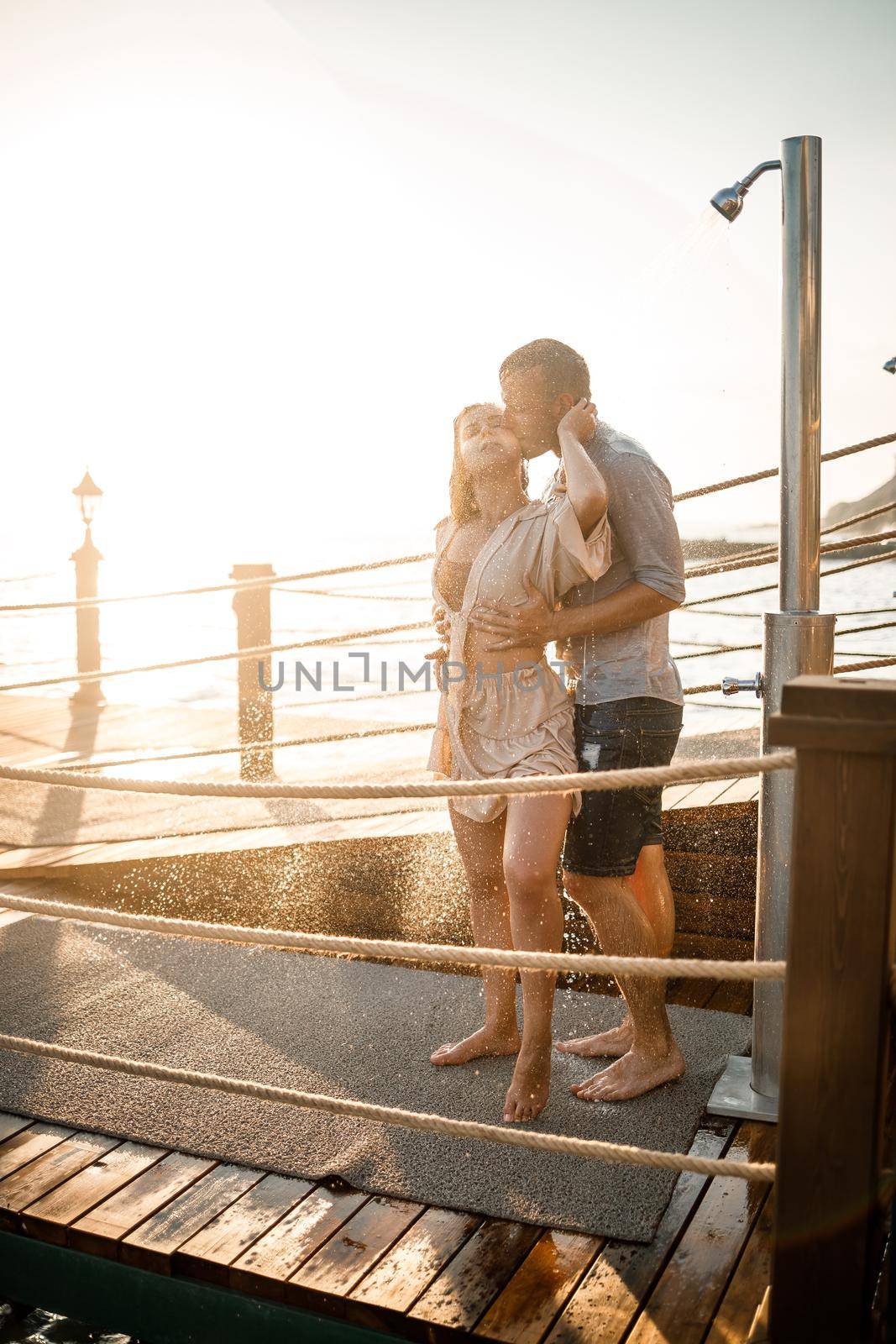 Happy couple by the sea. A guy and a girl are under the shower on an open-air pier. Happy couple on vacation. Man and woman by the sea. by Dmitrytph