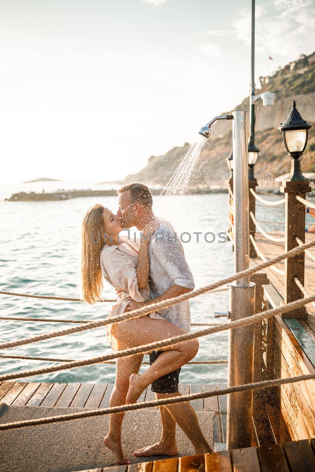 Happy couple by the sea. A guy and a girl are under the shower on an open-air pier. Happy couple on vacation. Man and woman by the sea.