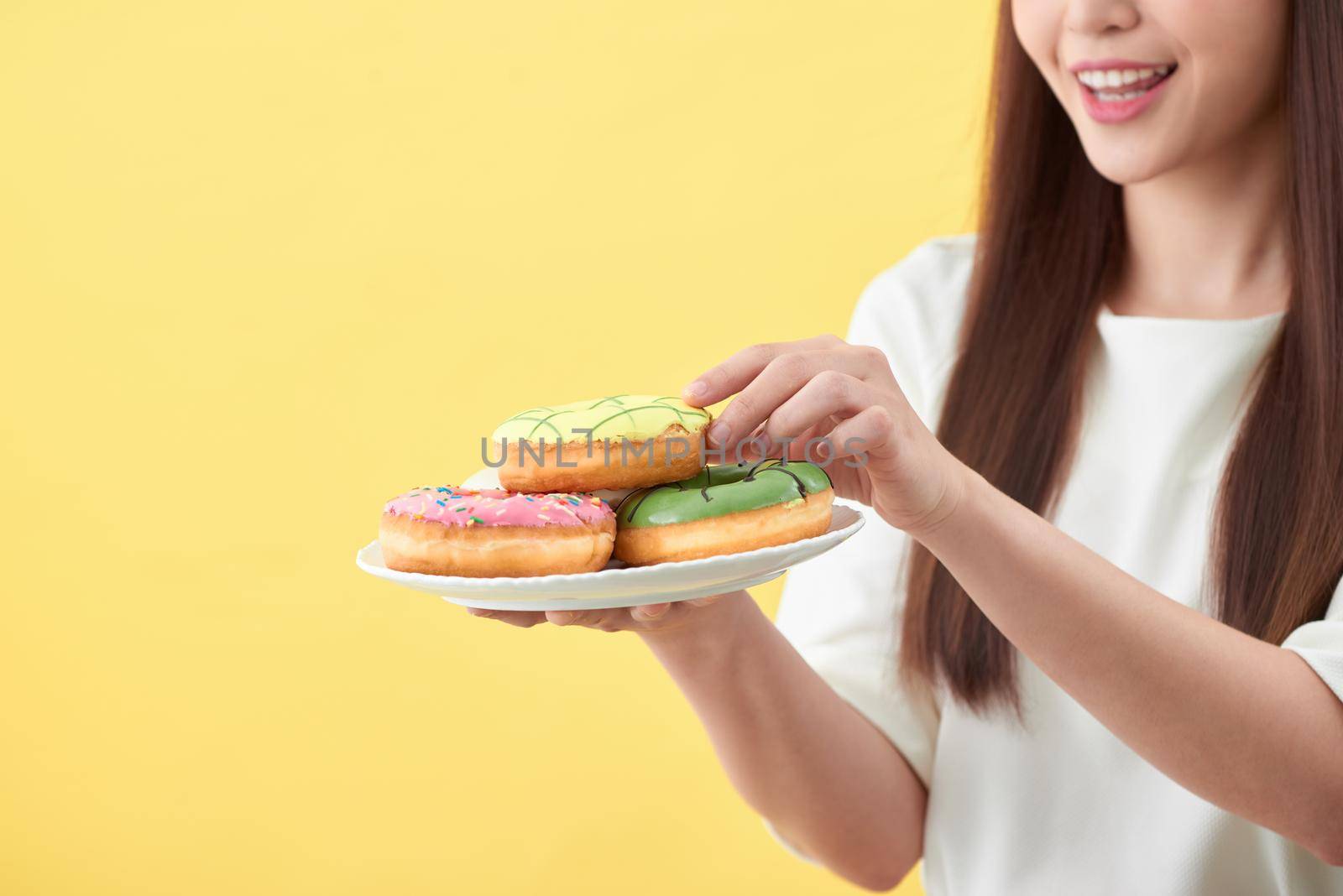 Beautiful young woman smiling holding a plate full of delicious color donuts 