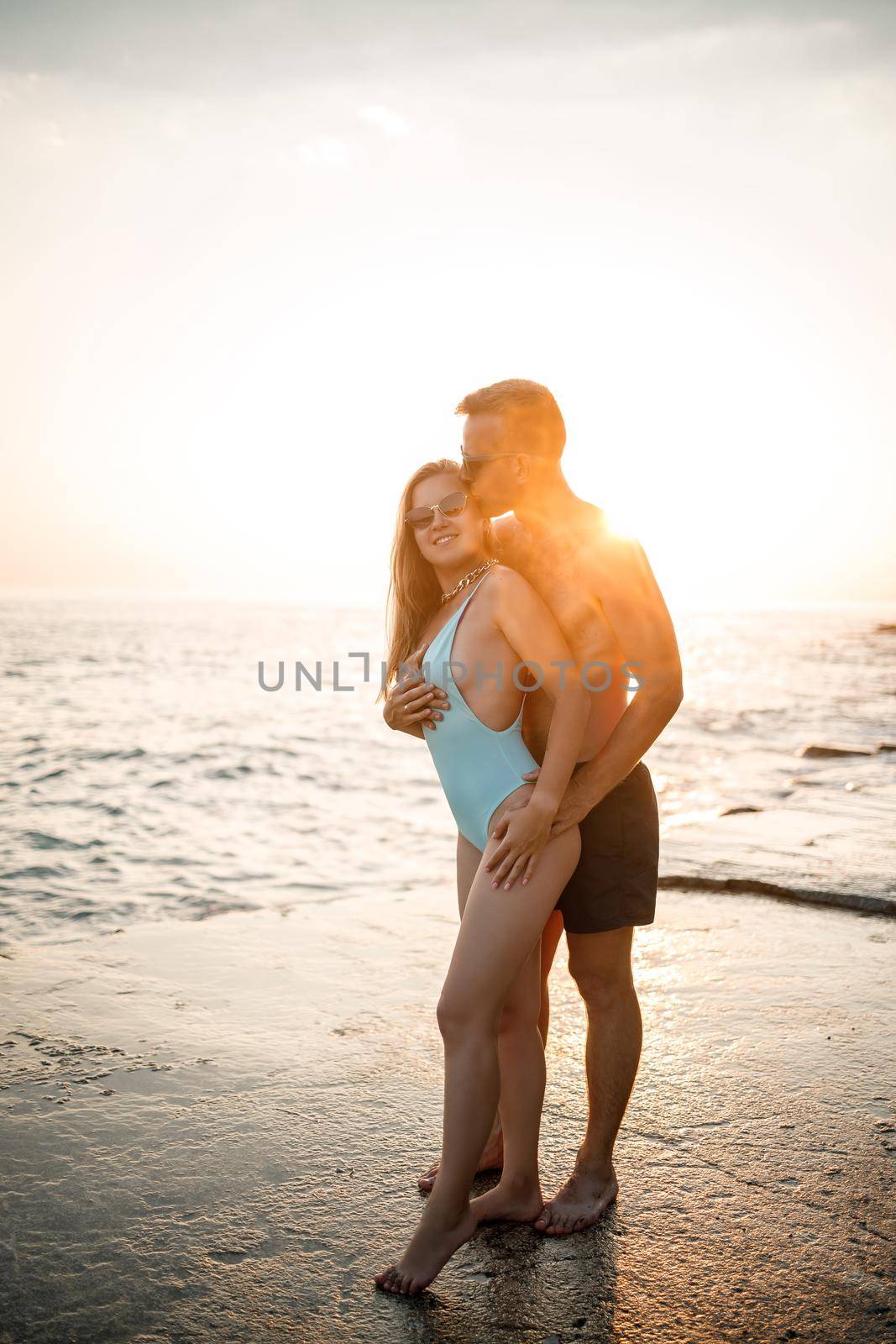 A loving couple walks along the beach by the sea. Young family at sunset by the Mediterranean Sea. Vacation concept. A woman in a swimsuit and a man in shorts at sunset by the sea. Selective focus.