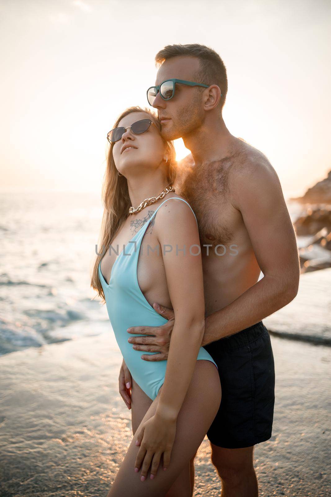 A loving couple walks along the beach by the sea. Young family at sunset by the Mediterranean Sea. Vacation concept. A woman in a swimsuit and a man in shorts at sunset by the sea. Selective focus.