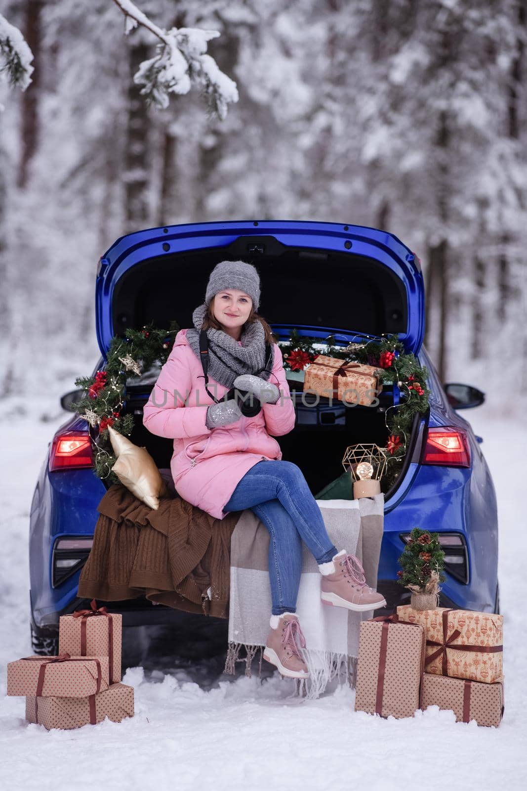 A woman in winter clothes drinks a hot drink sitting in a car decorated in a New Year's way. Traveling by car through the forest. A trip before Christmas.