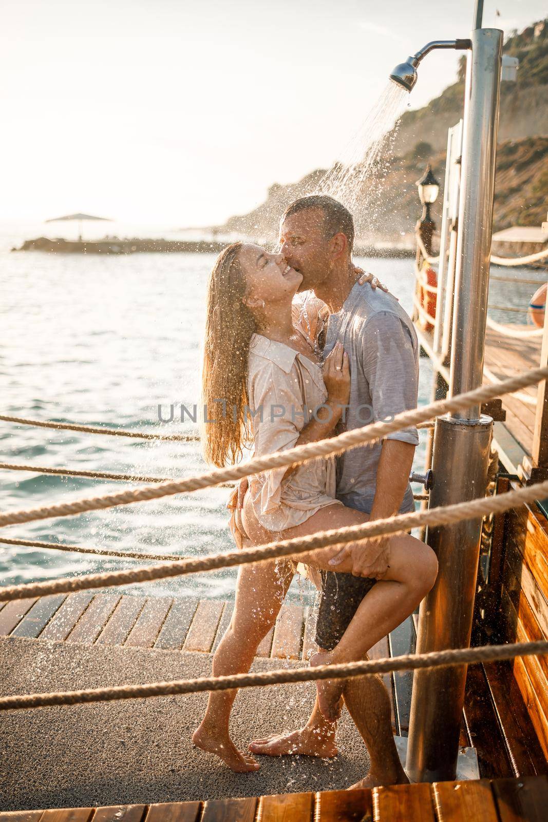 Happy couple by the sea. A guy and a girl are under the shower on an open-air pier. Happy couple on vacation. Man and woman by the sea. Selective focus by Dmitrytph