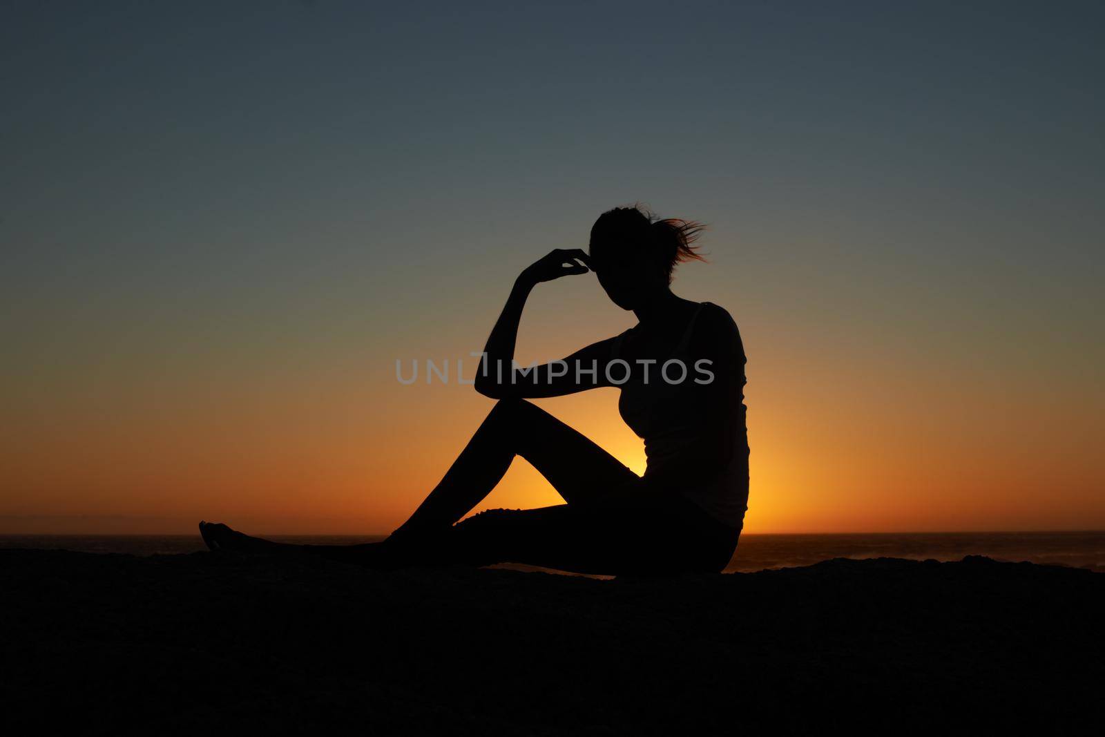 Having a rest a sunset. Silhouette of a young woman against a setting sun. by YuriArcurs