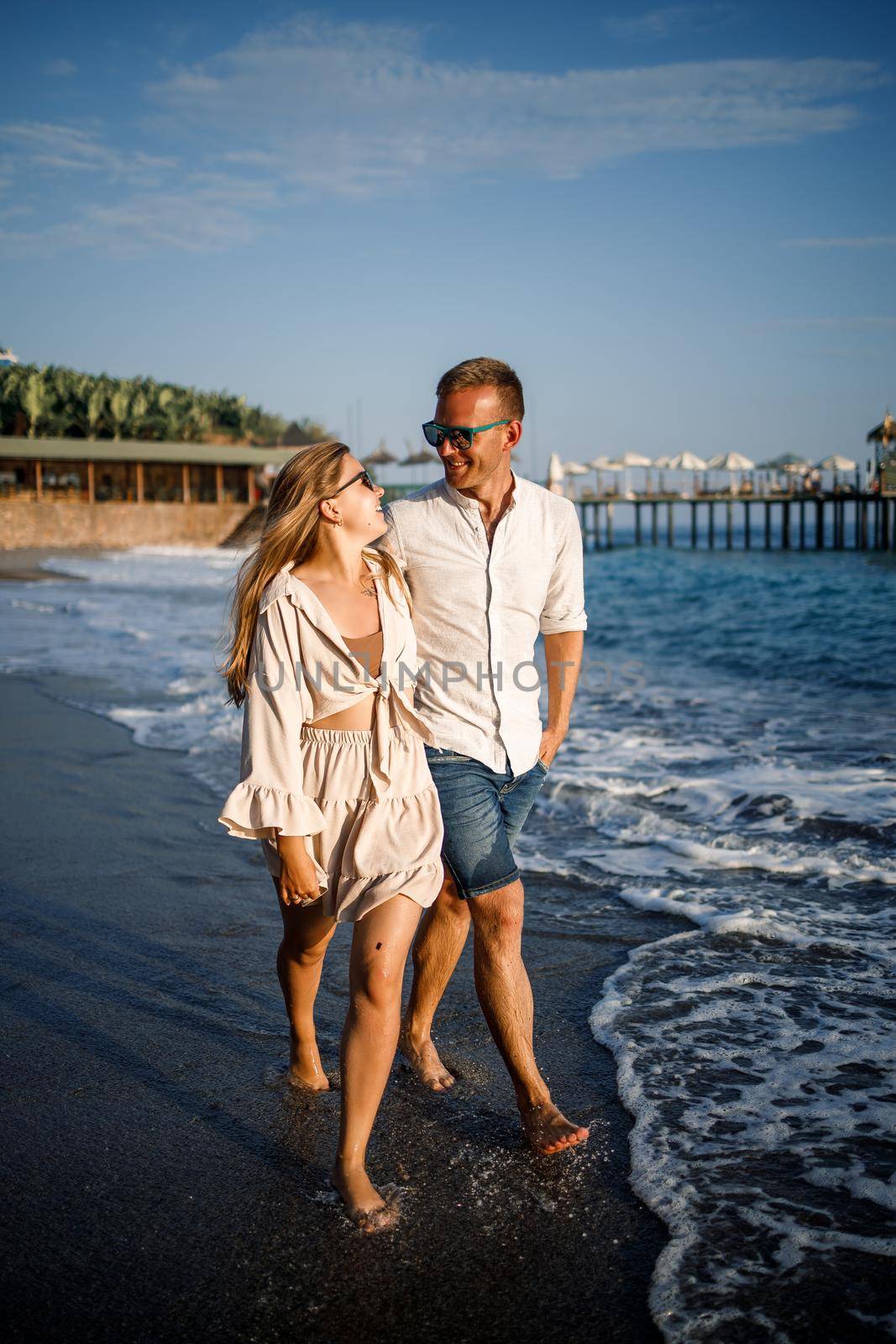 romantic young couple in love together on the sand walks along the beach of the Mediterranean sea. Summer vacation in a warm country.