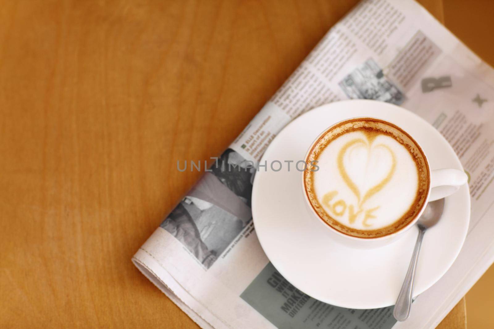Made with love...High angle shot of a lovingly prepared cup of cappuccino sitting on a newspaper. by YuriArcurs