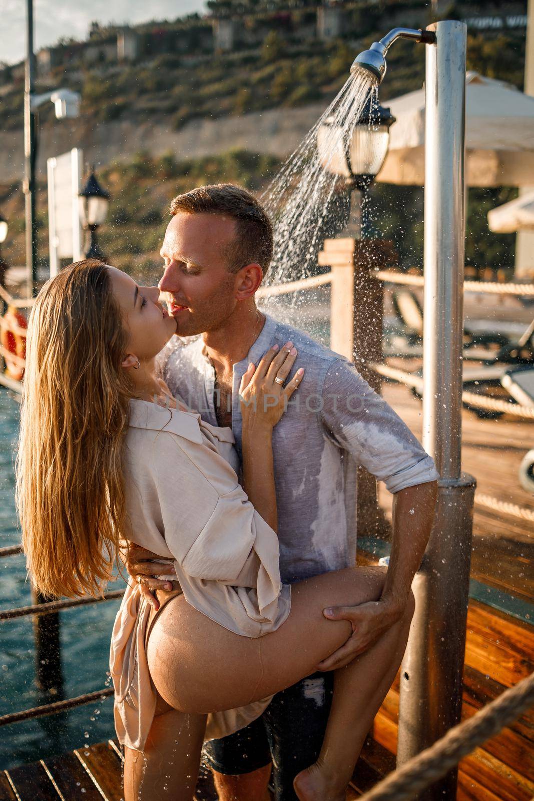 Happy couple by the sea. A guy and a girl are under the shower on an open-air pier. Happy couple on vacation. Man and woman by the sea.