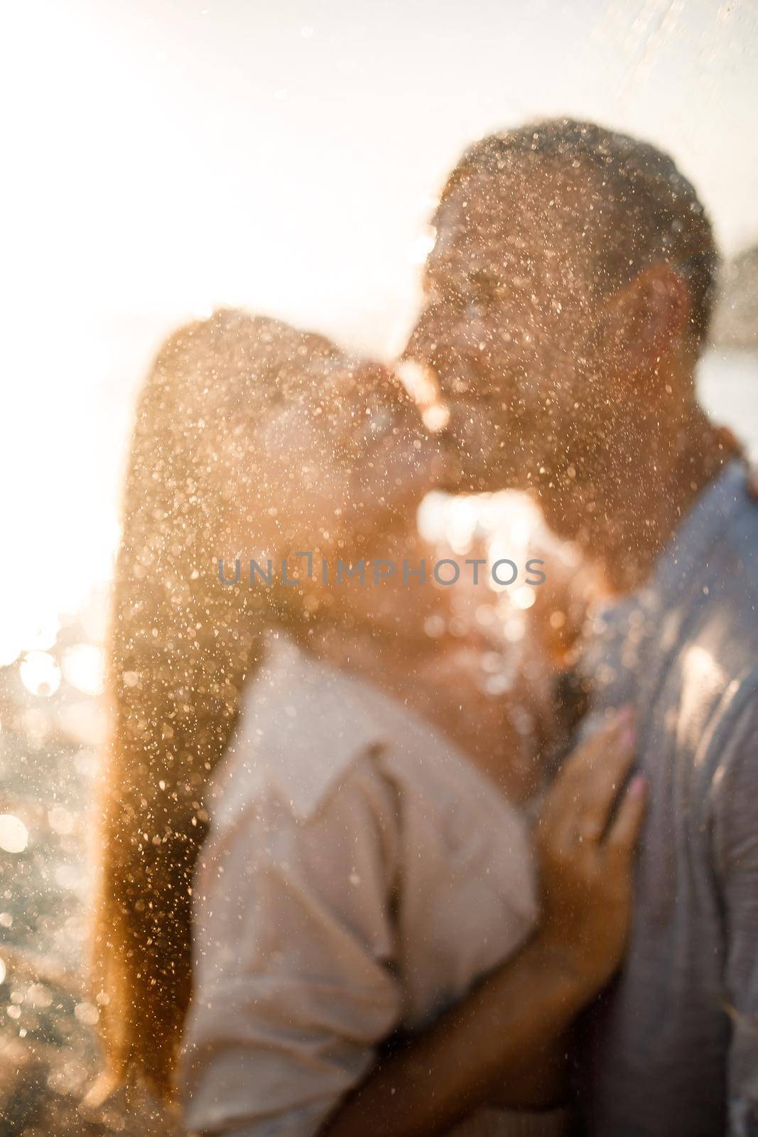 Beautiful couple in love hugs and kisses under the streams of water in a luxury spa hotel on their honeymoon, vacation in the tropics. Selective focus by Dmitrytph