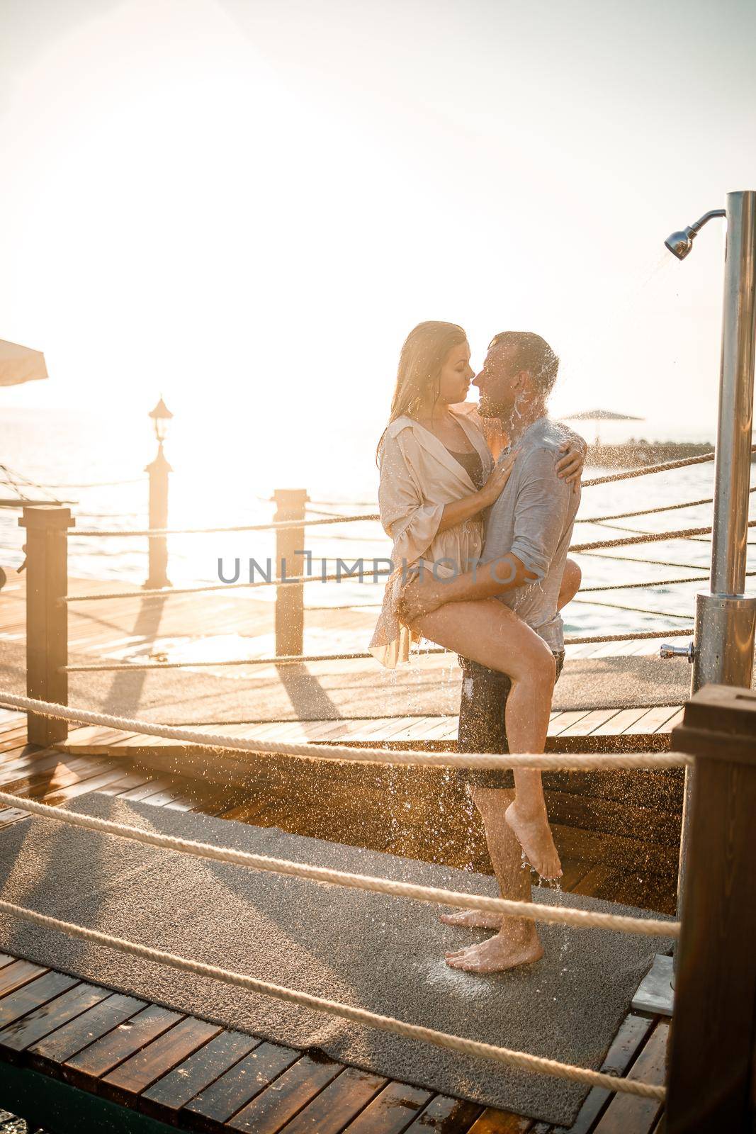 Happy couple by the sea. A guy and a girl are under the shower on an open-air pier. Happy couple on vacation. Man and woman by the sea. by Dmitrytph