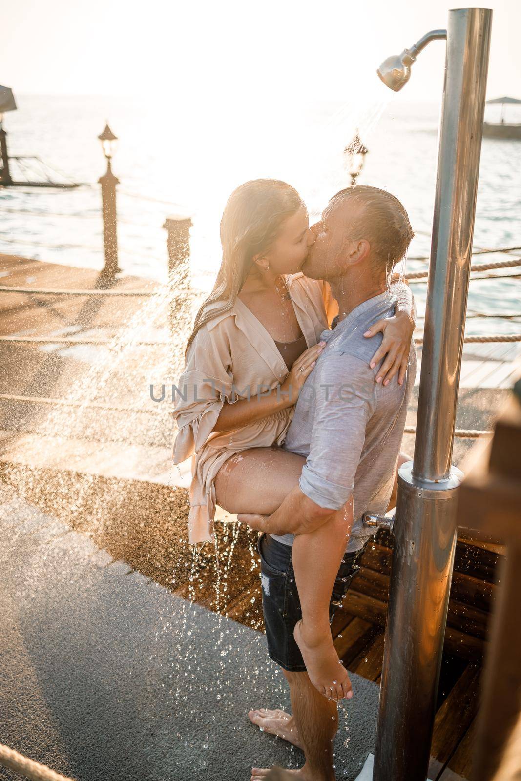 Happy couple by the sea. A guy and a girl are under the shower on an open-air pier. Happy couple on vacation. Man and woman by the sea.