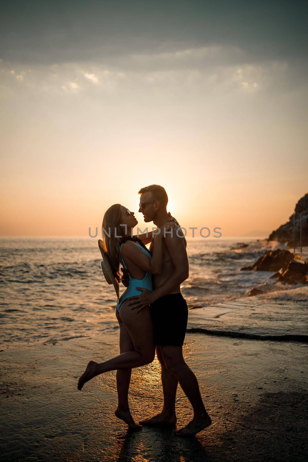 Beautiful couple in love on the background of the sunset by the sea. Young woman and man hugging by the sea at sunset by Dmitrytph