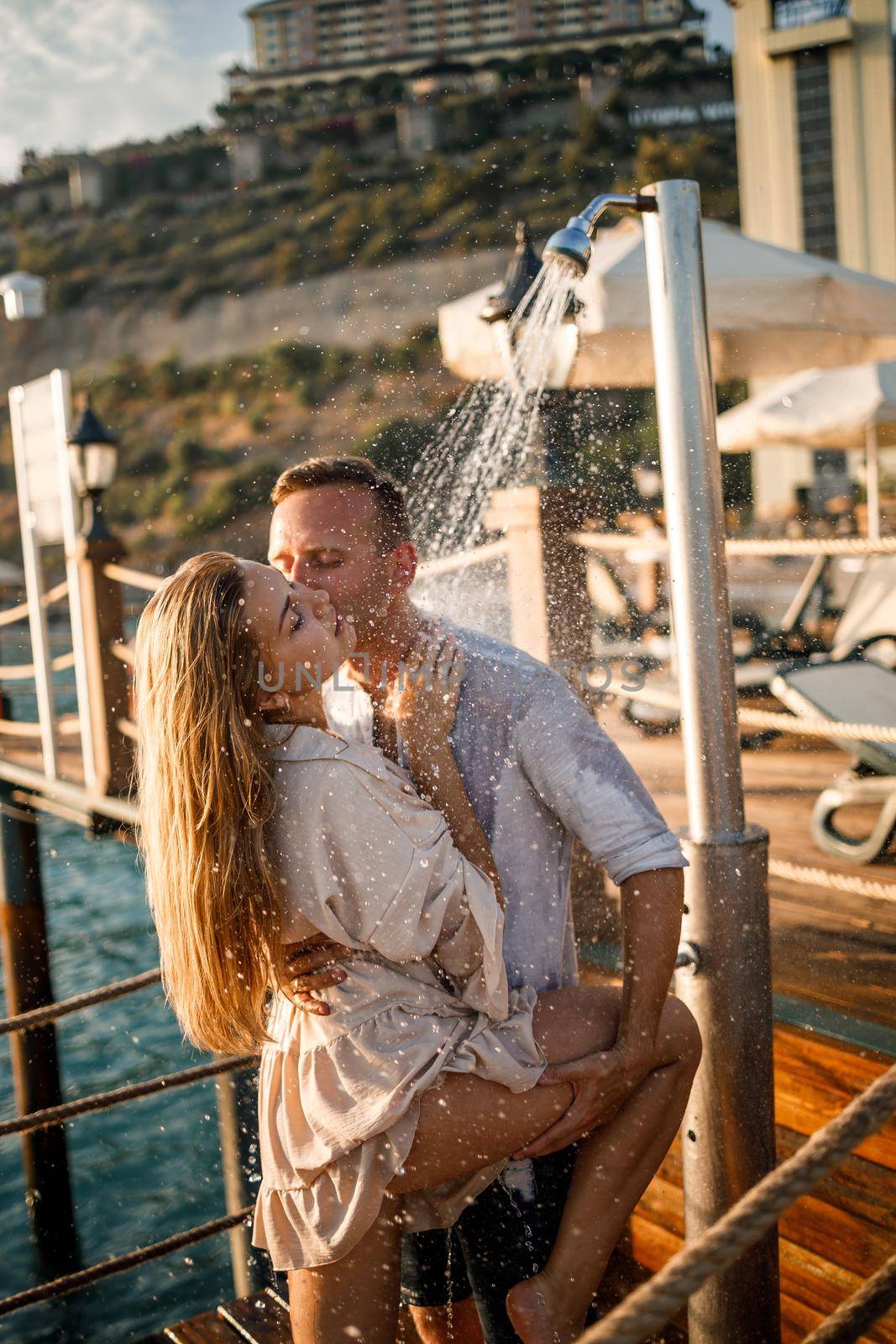 Happy couple by the sea. A guy and a girl are under the shower on an open-air pier. Happy couple on vacation. Man and woman by the sea. by Dmitrytph