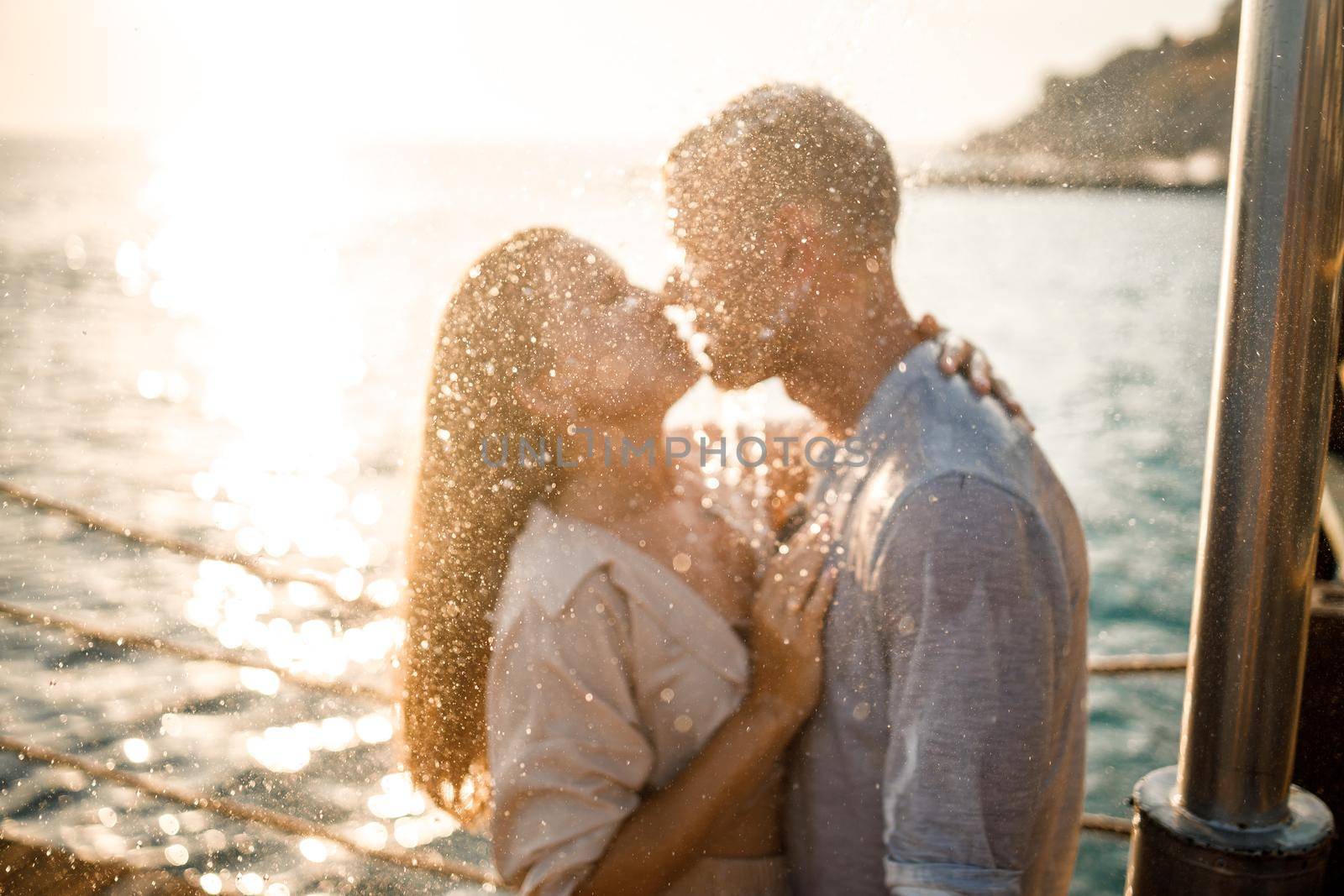 Beautiful couple in love hugs and kisses under the streams of water in a luxury spa hotel on their honeymoon, vacation in the tropics. Selective focus