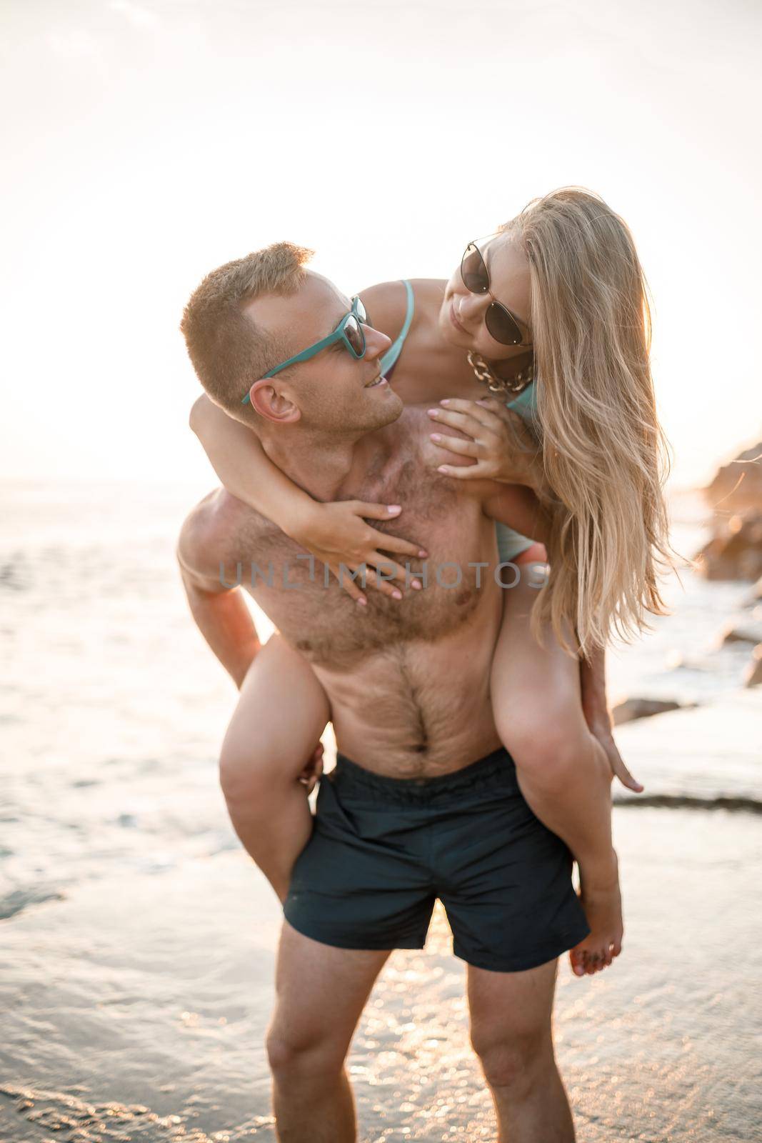 A loving couple walks along the beach by the sea. Young family at sunset by the Mediterranean Sea. Vacation concept. A woman in a swimsuit and a man in shorts at sunset by the sea. Selective focus.