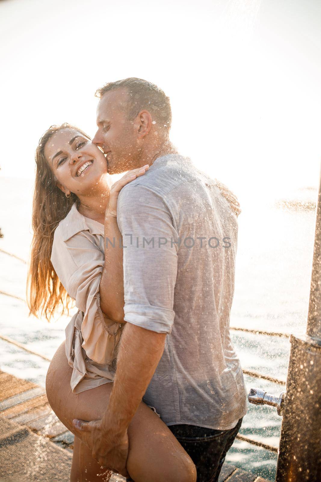 Beautiful couple in love hugs and kisses under the streams of water in a luxury spa hotel on their honeymoon, vacation in the tropics. Selective focus by Dmitrytph