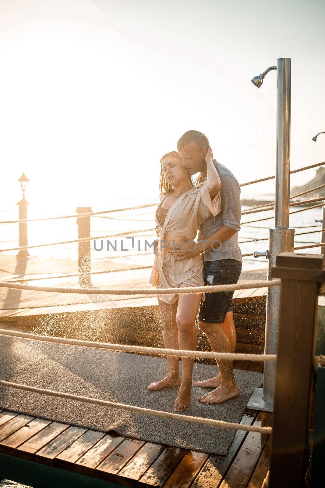 Happy couple by the sea. A guy and a girl are under the shower on an open-air pier. Happy couple on vacation. Man and woman by the sea.