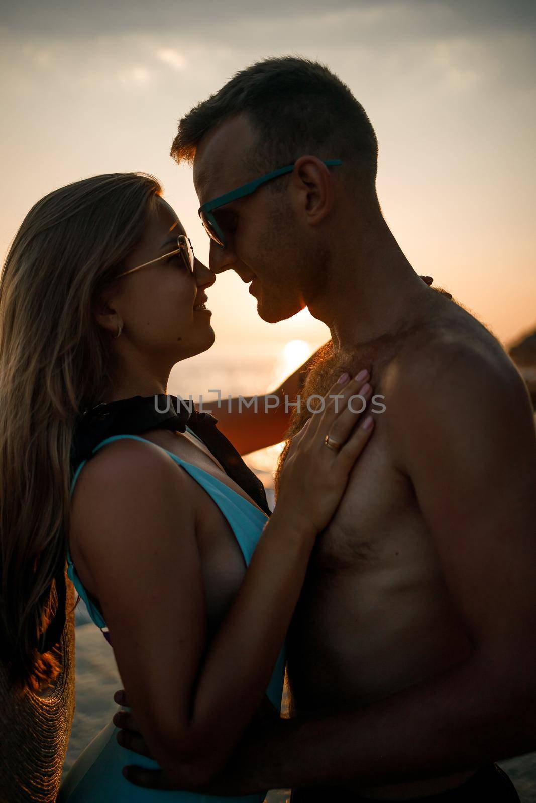 Beautiful couple in love on the background of the sunset by the sea. Young woman and man hugging by the sea at sunset by Dmitrytph