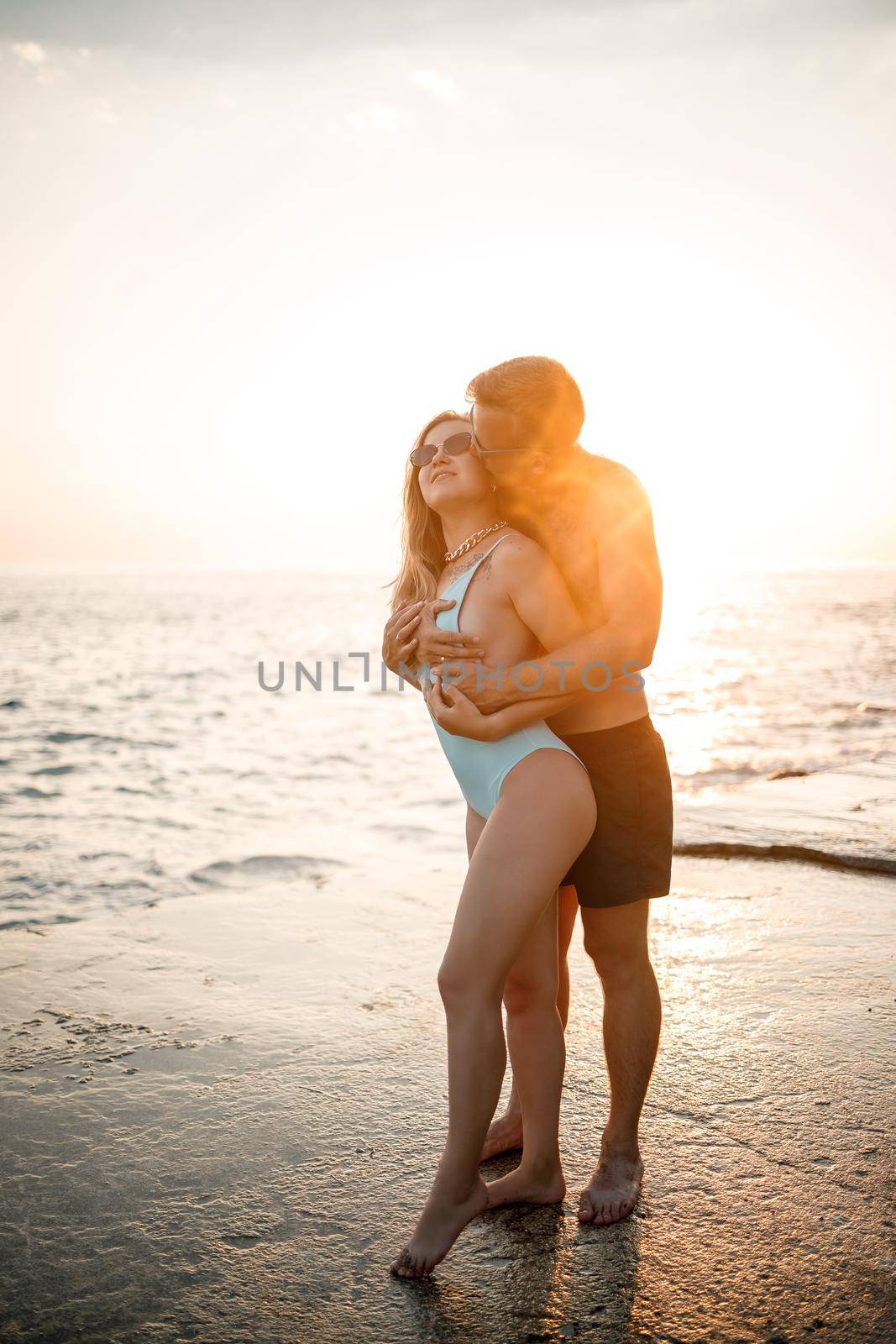 A loving couple walks along the beach by the sea. Young family at sunset by the Mediterranean Sea. Vacation concept. A woman in a swimsuit and a man in shorts at sunset by the sea. Selective focus.