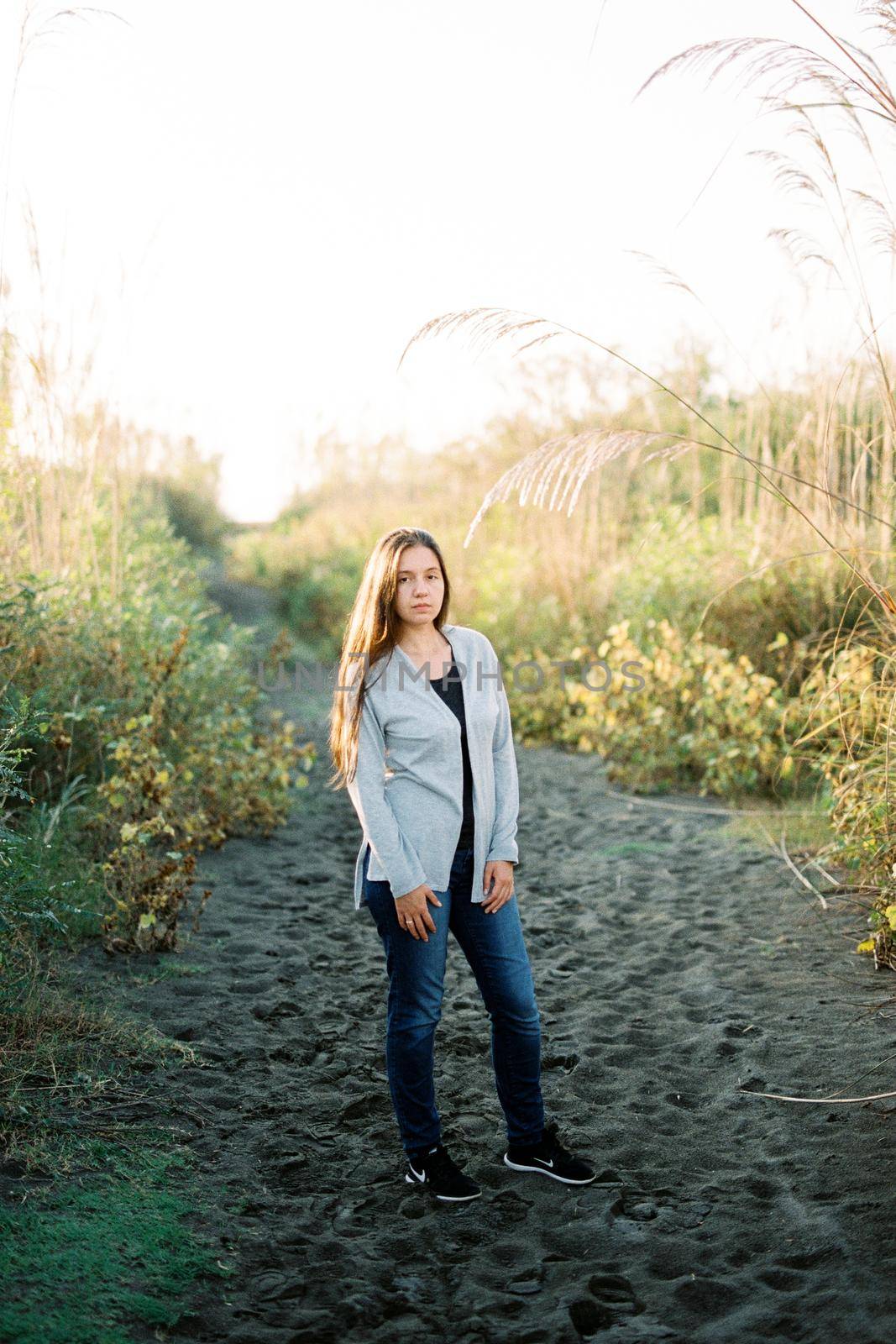 Young woman in a long sweater stands on a sandy road in the park. High quality photo