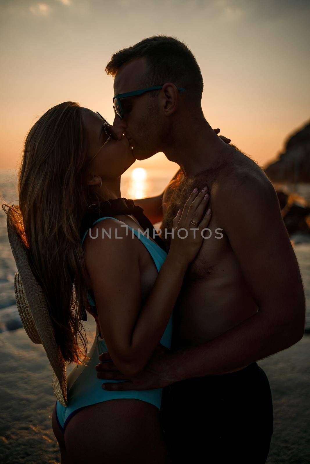 Beautiful couple in love on the background of the sunset by the sea. Young woman and man hugging by the sea at sunset