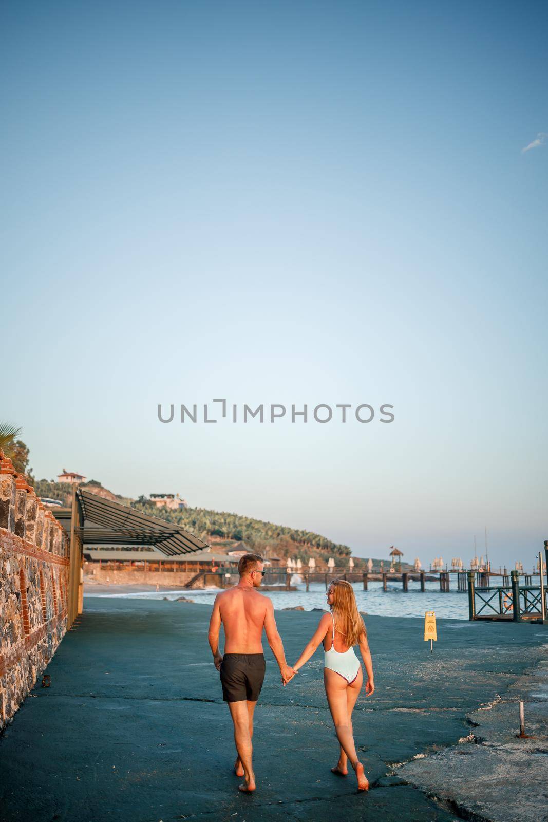 Romantic young couple in love walking together at sunset along the Mediterranean beach. Summer vacation in a warm country. Happy married couple on vacation in Turkey. Selective focus