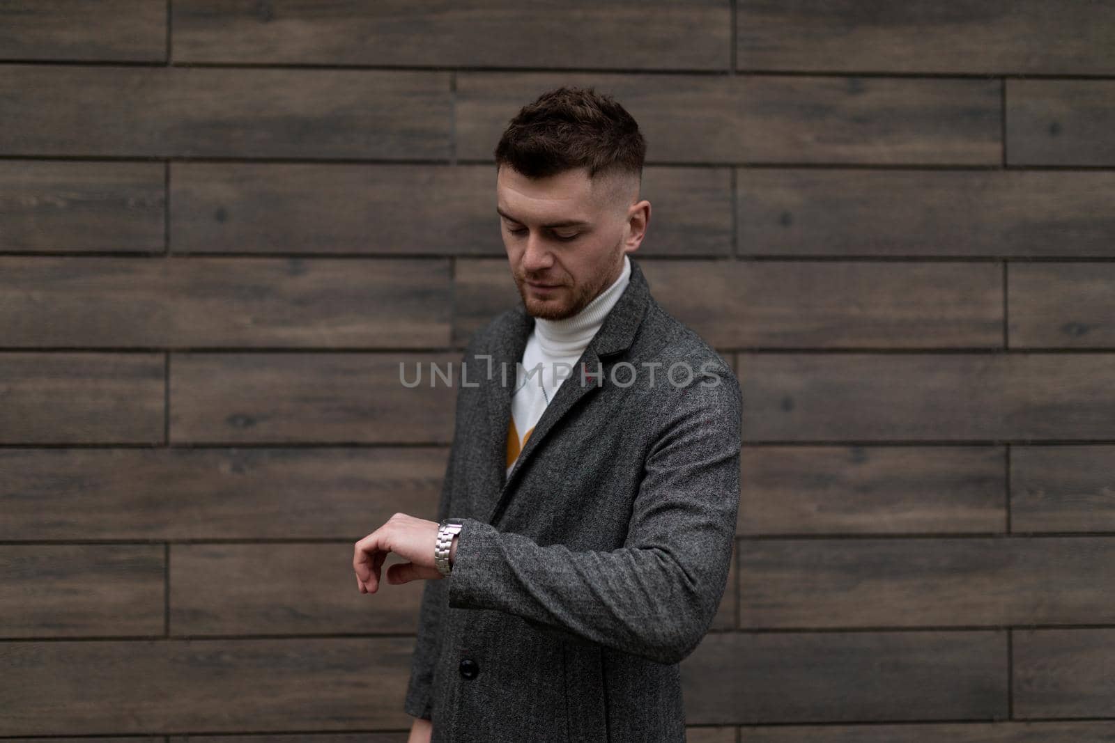 stylish young brutal male businessman on the background of the wall of the building looks at his watch.