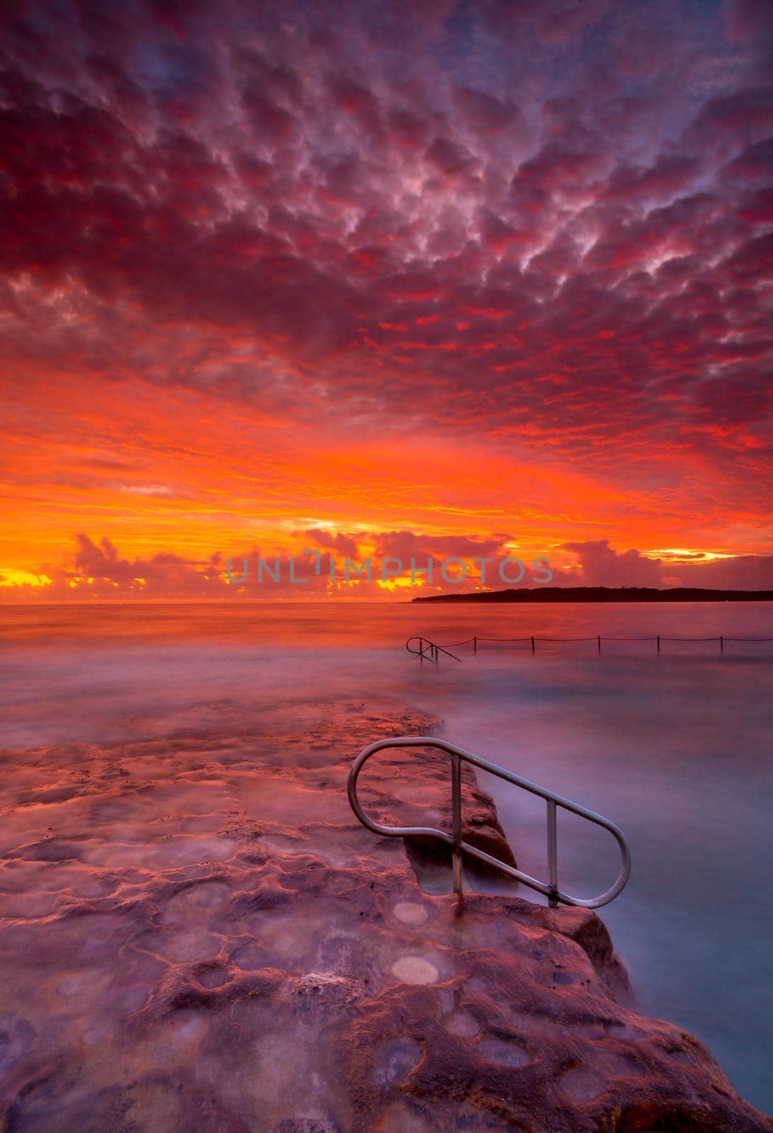 Rich red vibrant and stunning sunrise over rock pool and ocean in Cronulla, Australia