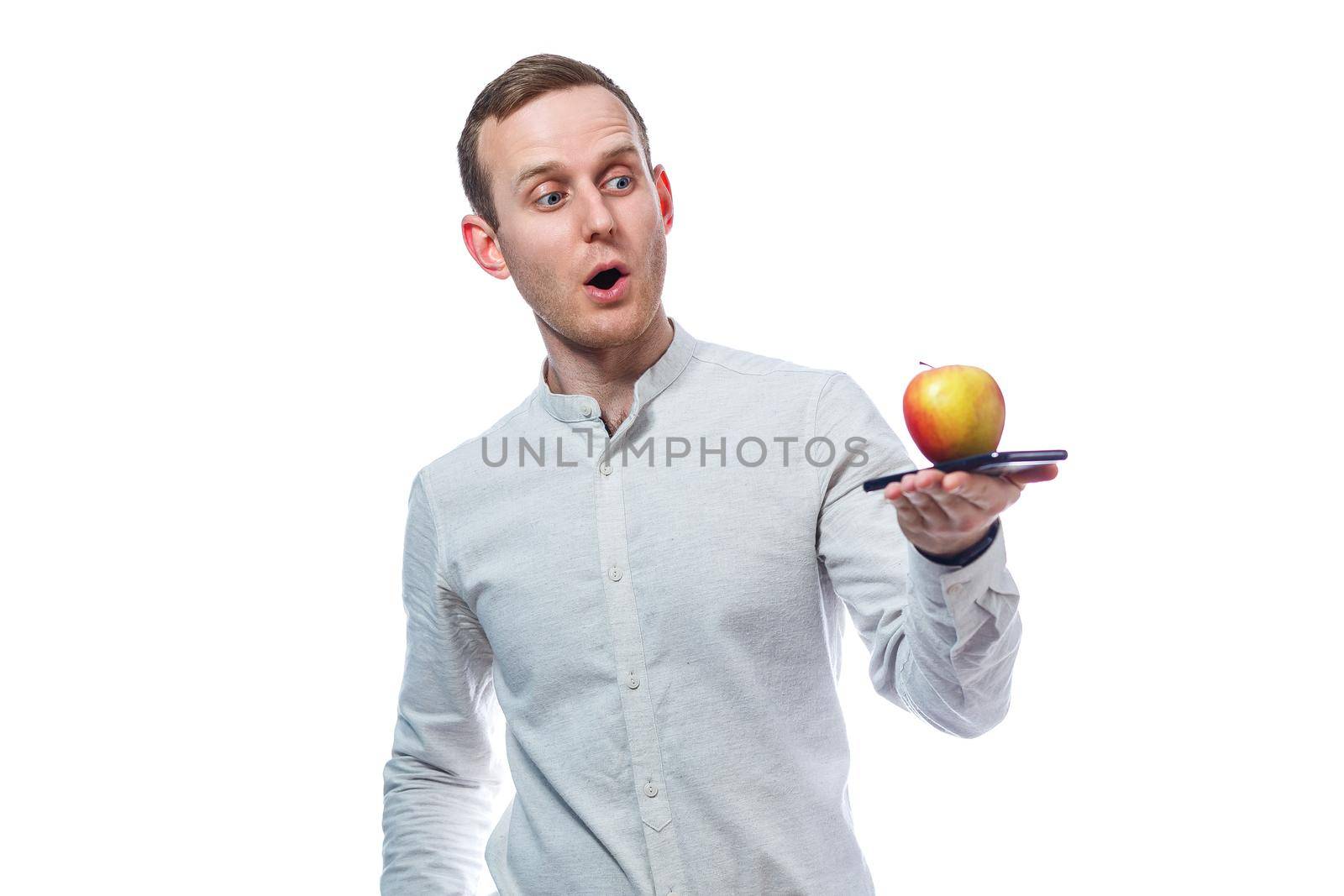 Caucasian male businessman holding a mobile phone in black and holding a red-yellow apple. He is wearing a shirt. Emotional portrait. Isolated on white background by Dmitrytph