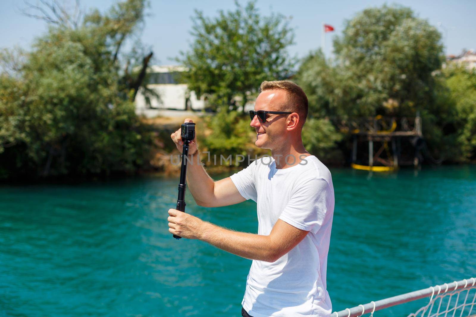 A man in a white T-shirt holds an action camera in his hands and shoots a beautiful view of the sea