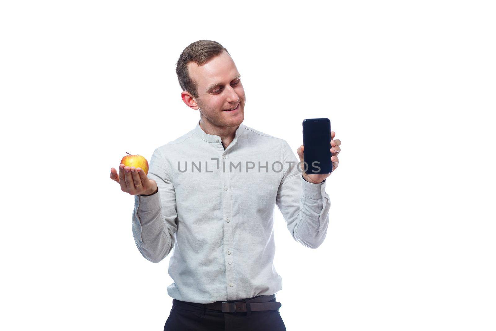 Caucasian male businessman holding a mobile phone in black and holding a red-yellow apple. He is wearing a shirt. Emotional portrait. Isolated on white background