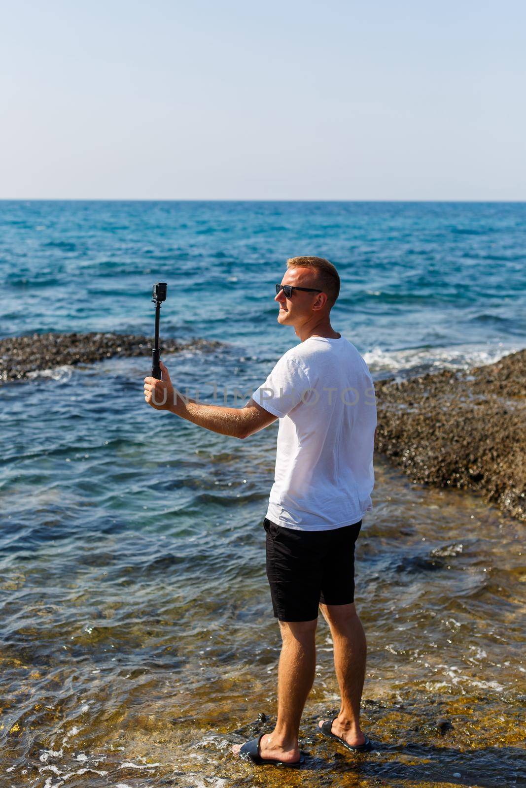 A man in a white T-shirt holds an action camera in his hands and shoots a beautiful view of the sea