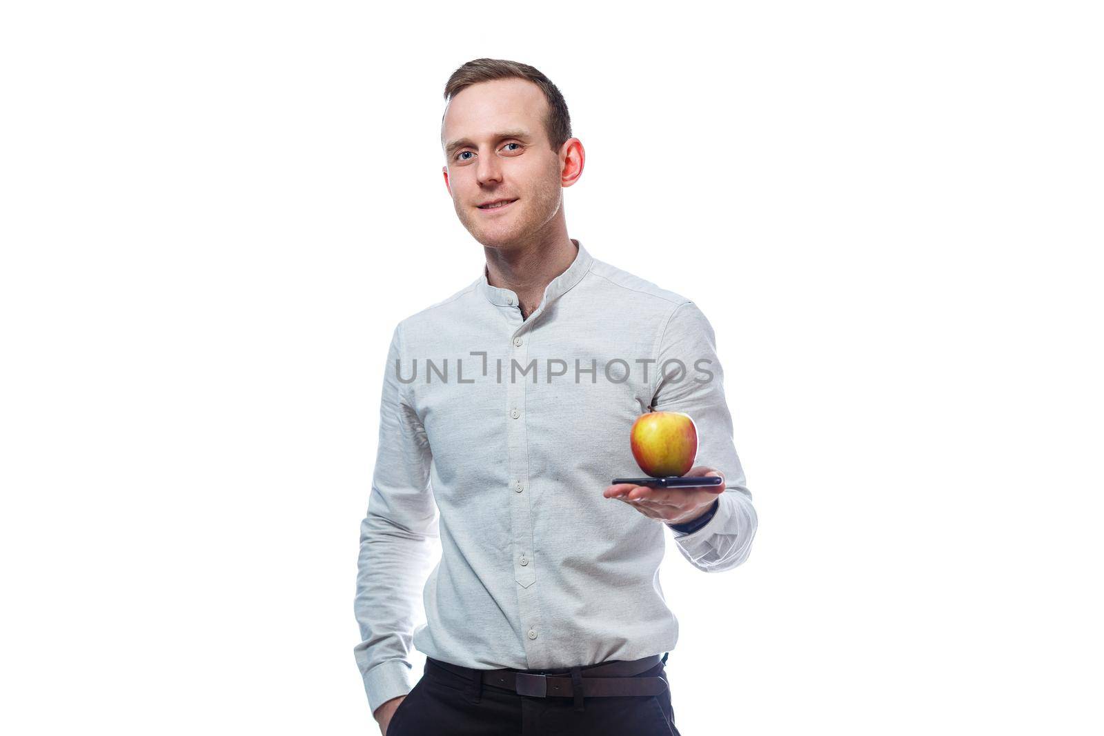 Caucasian male businessman holding a mobile phone in black and holding a red-yellow apple. He is wearing a shirt. Emotional portrait. Isolated on white background by Dmitrytph