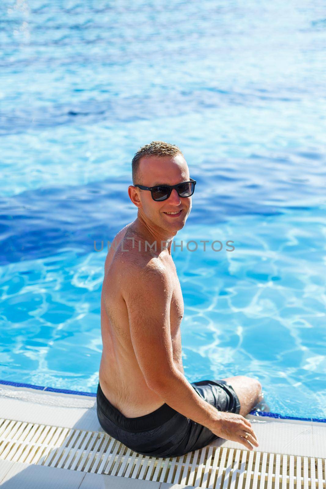 Young attractive man in sunglasses is resting in the pool on summer vacation. The guy in the pool by the hotel