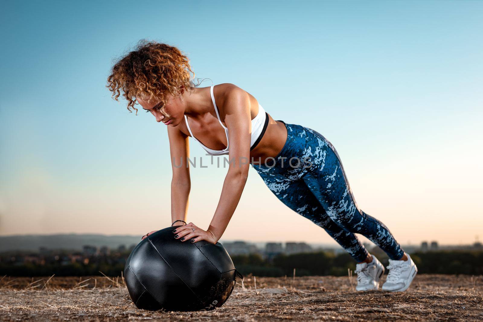 Young fitness woman doing push-ups on the wall ball in a sunset.