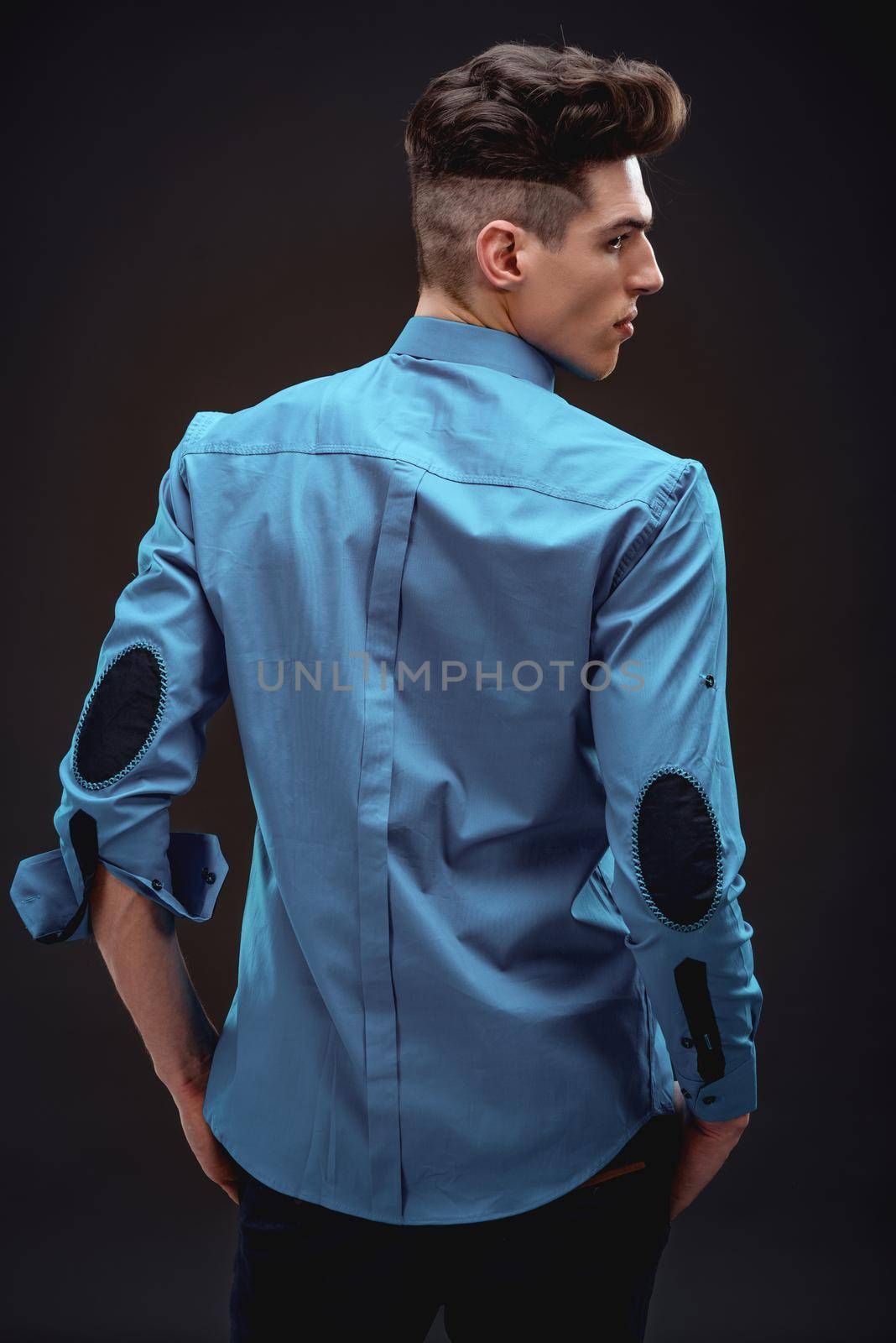 Rear view of a handsome fashionable man in turquoise shirt. Black background. 
