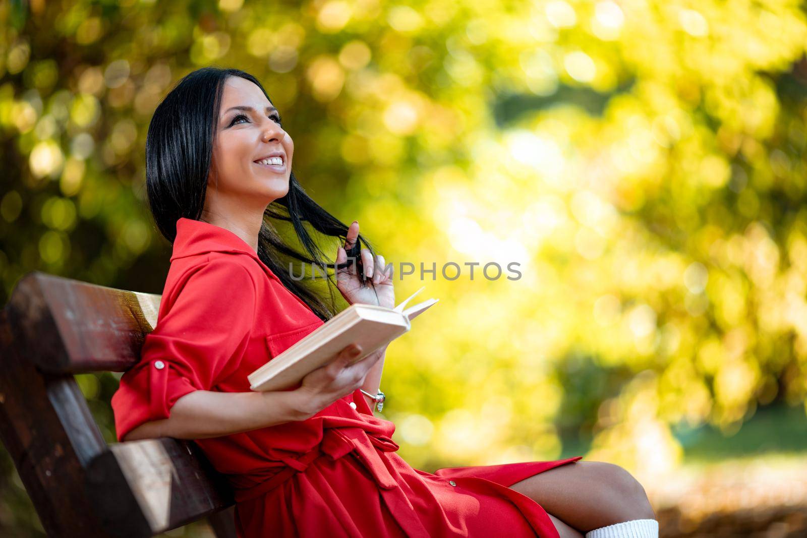 Beautiful young woman enjoying in spring colors sunny forest looking away and holding a book in her hand.  
